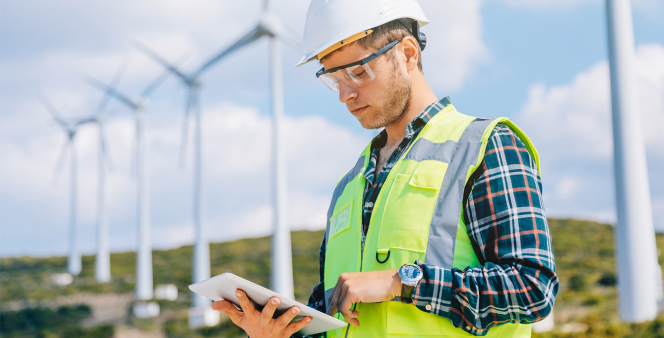 Ingenieur betrachtet Dokumente, Windkraftanlagen im Hintergrund (Foto)